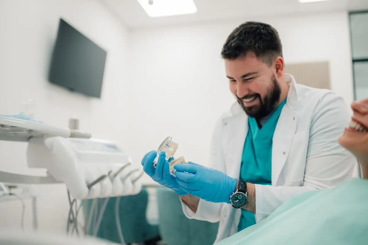 A smiling man holds a dental tool, showcasing his expertise in denture services and patient care.