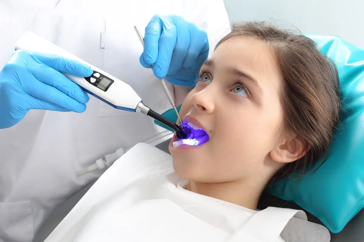 Dentist using a curing light on a young girl's tooth in a dental office.