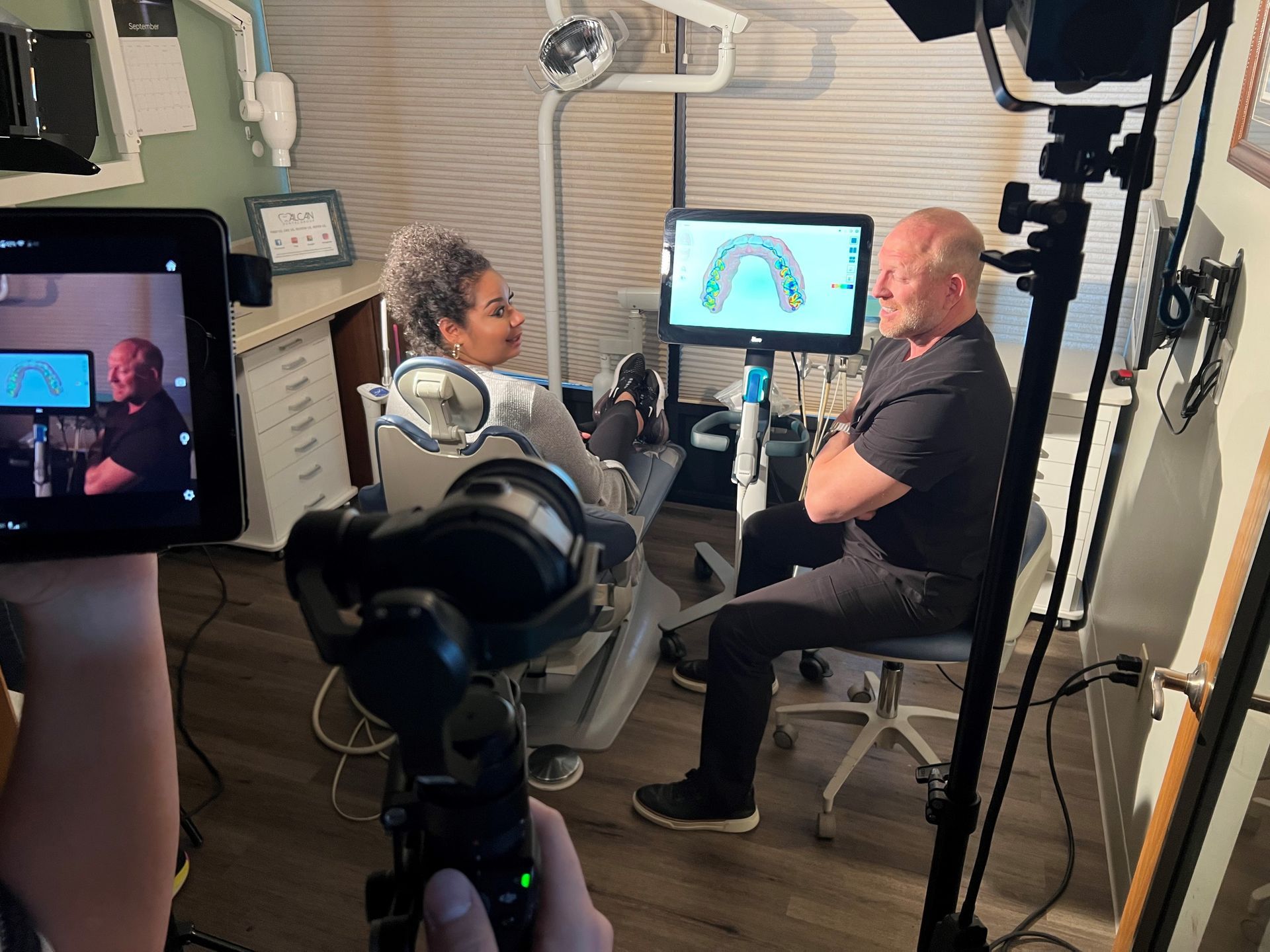 A dentist consulting with a patient about teeth imaging in a dental office; filming is underway.